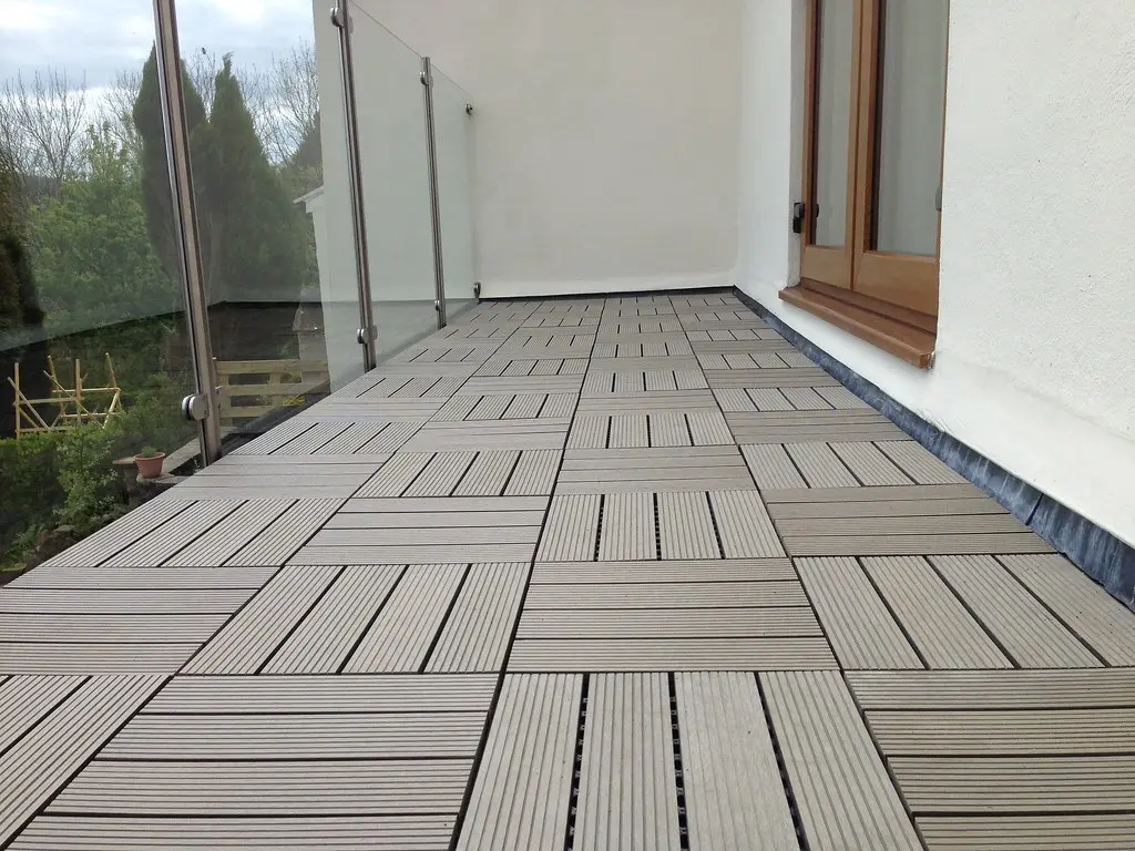 Hands lifting an interlocking balcony deck tile to reveal the reversible base on concrete