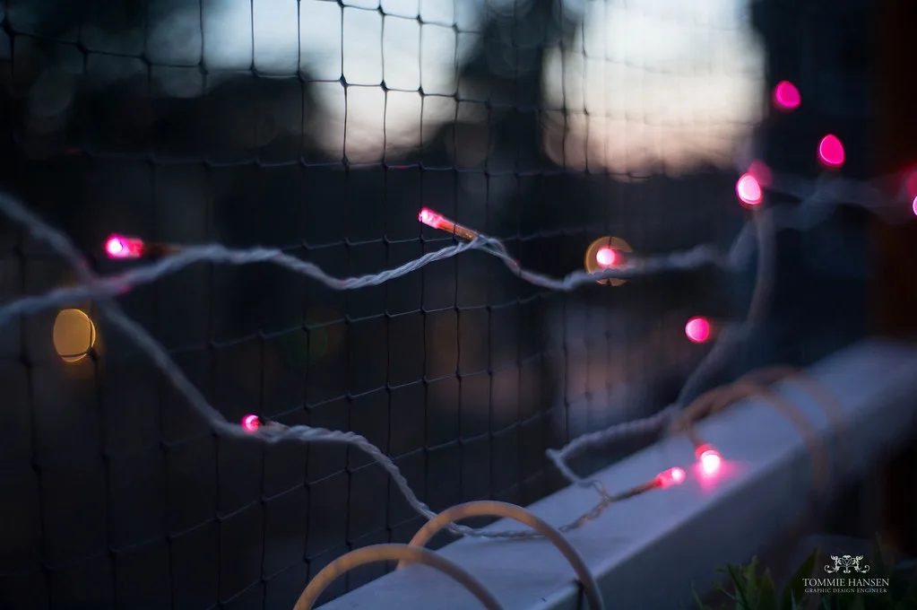 Hands clipping a warm LED light to a balcony rail beside a potted plant