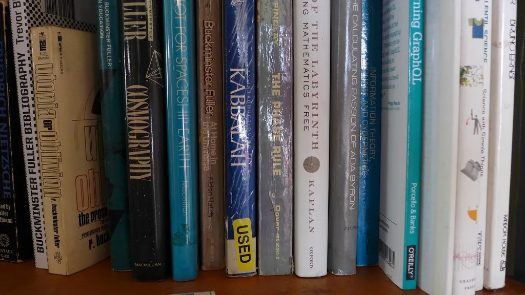 Close-up of a bookshelf shelf styled with stacked books, a vase, and framed decor.