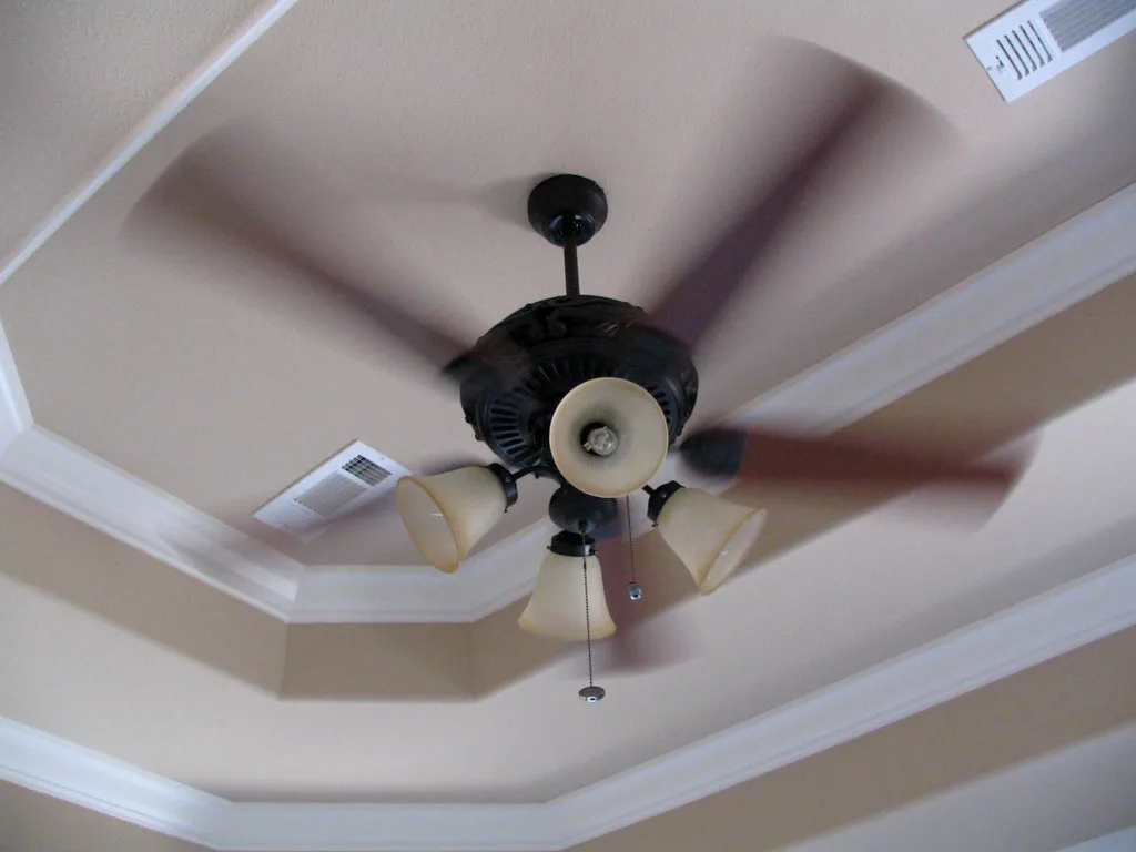 Hand measuring a ceiling fan blade span near a ceiling mount in a living room