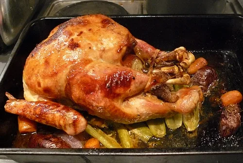 Roasting pan rack lifting a browned turkey above drippings beside a baster
