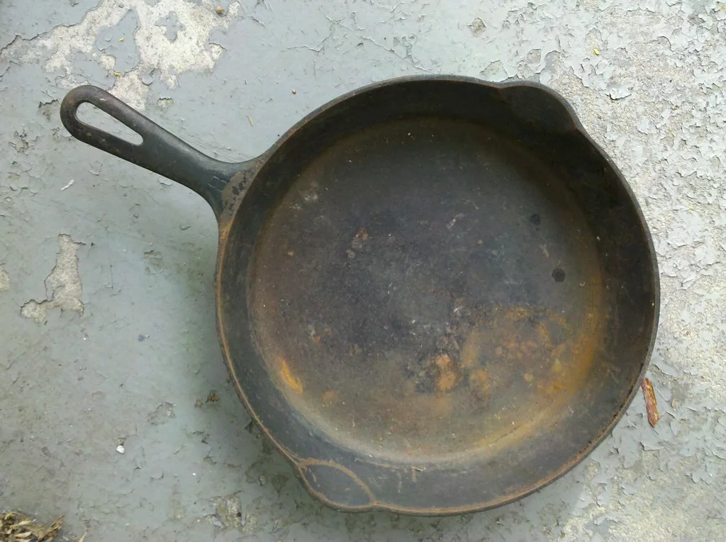 Hand wiping a cast iron skillet with oil to restore a smooth seasoned surface