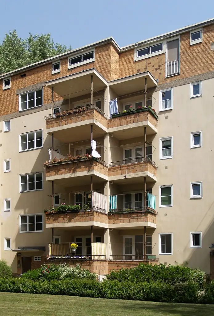 Hands clipping a balcony privacy screen to a railing as evening light shows the woven fabric
