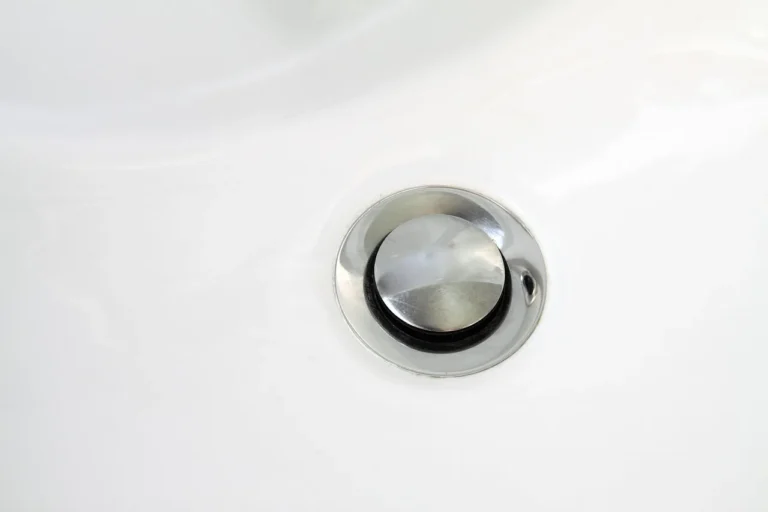 Homeowner inspecting a bathroom sink drain and P-trap under the vanity as water pools in the basin
