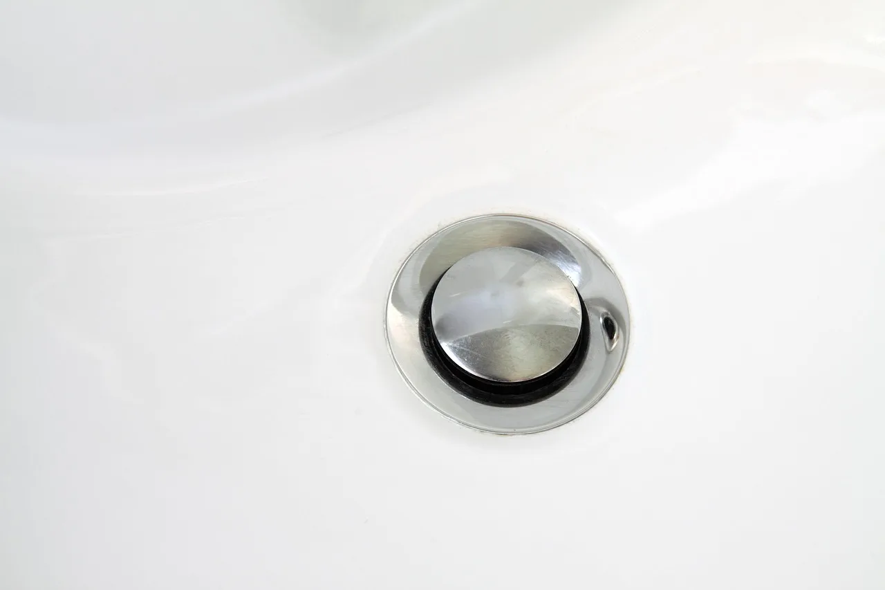 Homeowner inspecting a bathroom sink drain and P-trap under the vanity as water pools in the basin