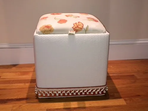Open storage ottoman filled with folded blankets and pillows beside a bed in natural light.