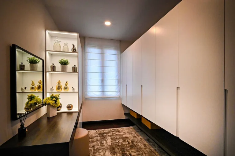 A small bedroom with a wardrobe, under-bed drawers, and open shelving in natural light.