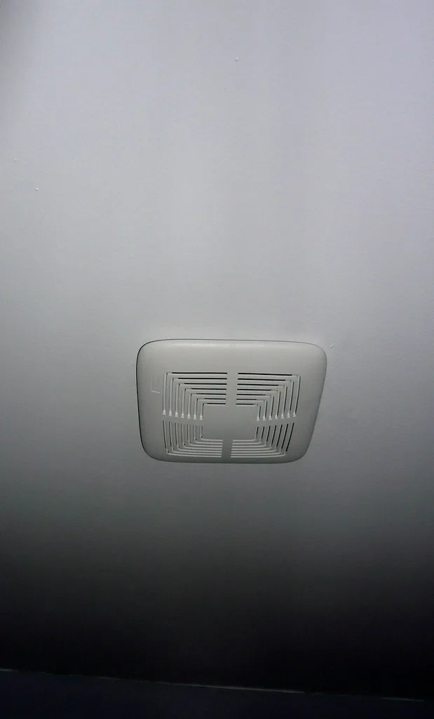 Bathroom exhaust fan grille beside a tape measure and duct on a workbench