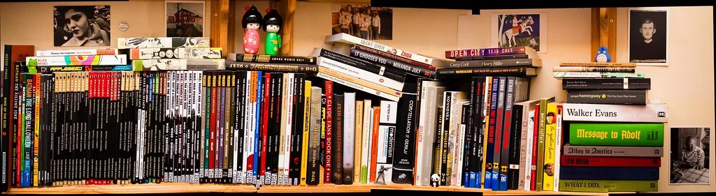 Close-up of a hand styling a modern bookshelf with books, a vase, and a plant