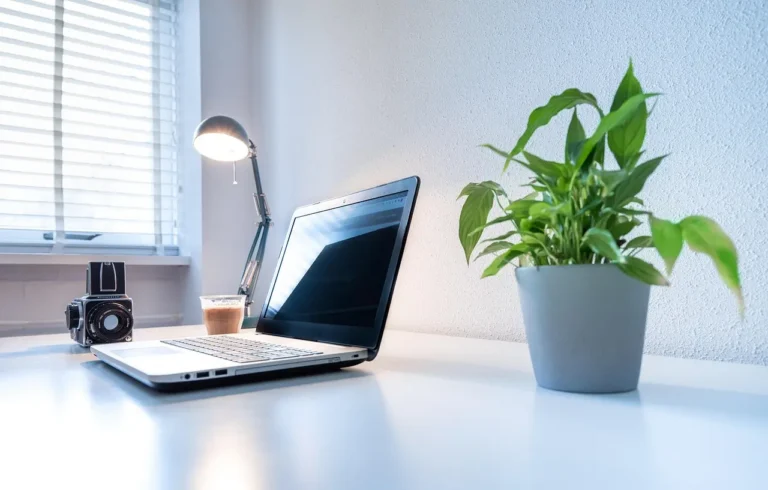 Desk lamp on a home office desk beside a laptop, monitor, notebook, and coffee mug in natural light
