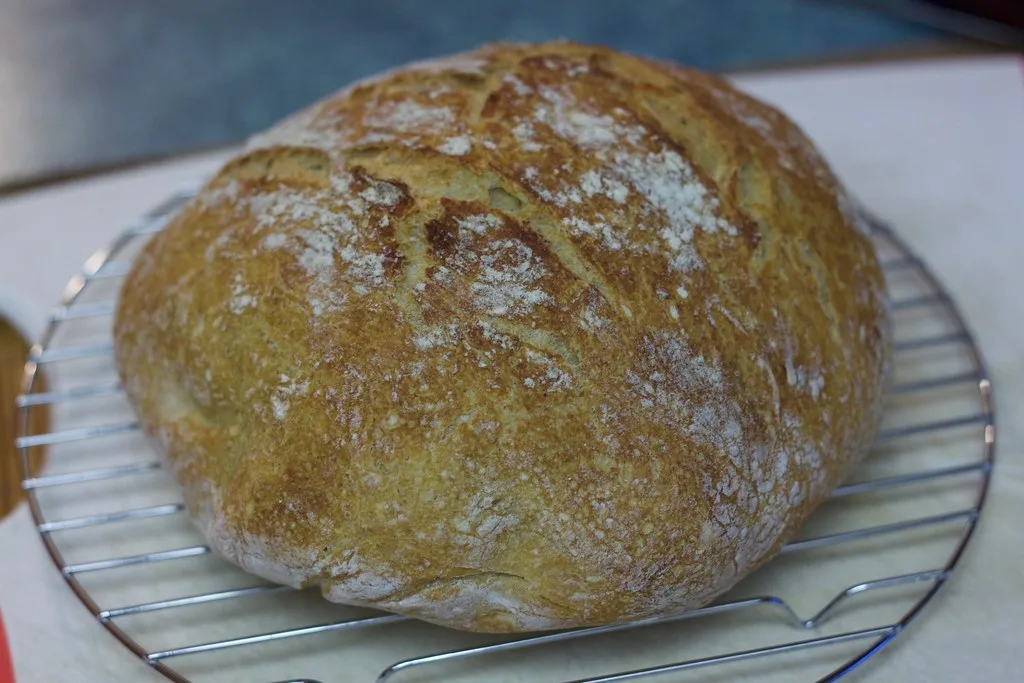 Sourdough loaf lowered into a hot Dutch oven with parchment paper and steam