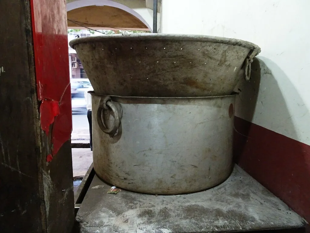 Hand opening a large pot of biryani with steam rising over the rice