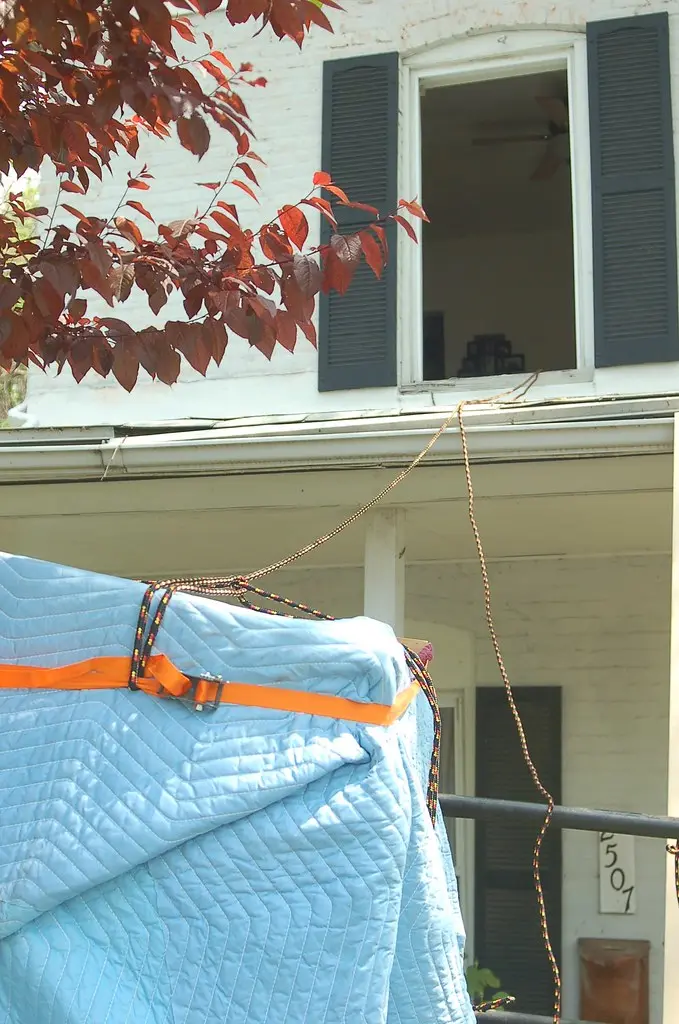 Close-up of moving straps supporting a sofa as gloved hands adjust the lift points.