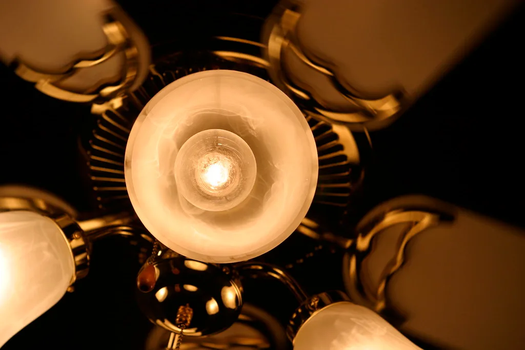 Close-up of a bright ceiling fan light fixture with frosted shade in a bedroom