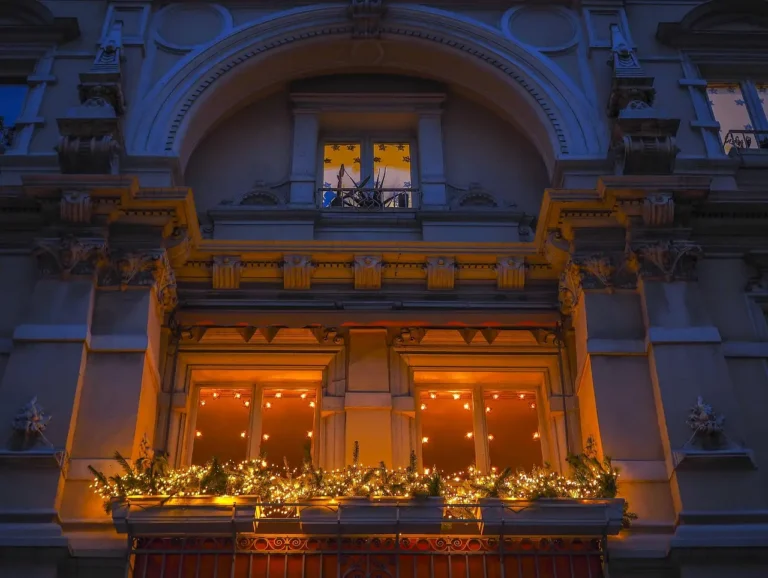 Small apartment balcony with a slim Christmas garland, lanterns, a tiny evergreen, and compact furniture