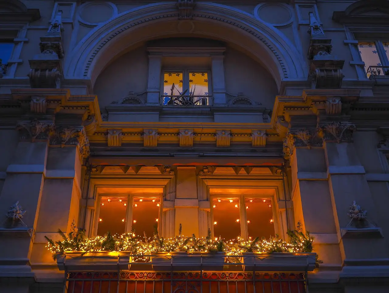Small apartment balcony with a slim Christmas garland, lanterns, a tiny evergreen, and compact furniture