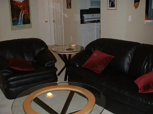 Side table beside an armchair holding a lamp, book, and drink in a bright room