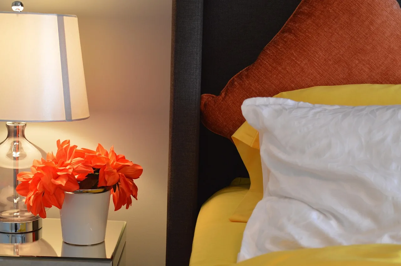 A cozy bedroom with a bedside lamp and wall dimmer switch in warm evening light