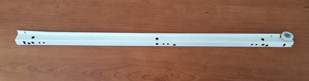 Drawer slide samples on a workbench beside an open cabinet and measuring tools