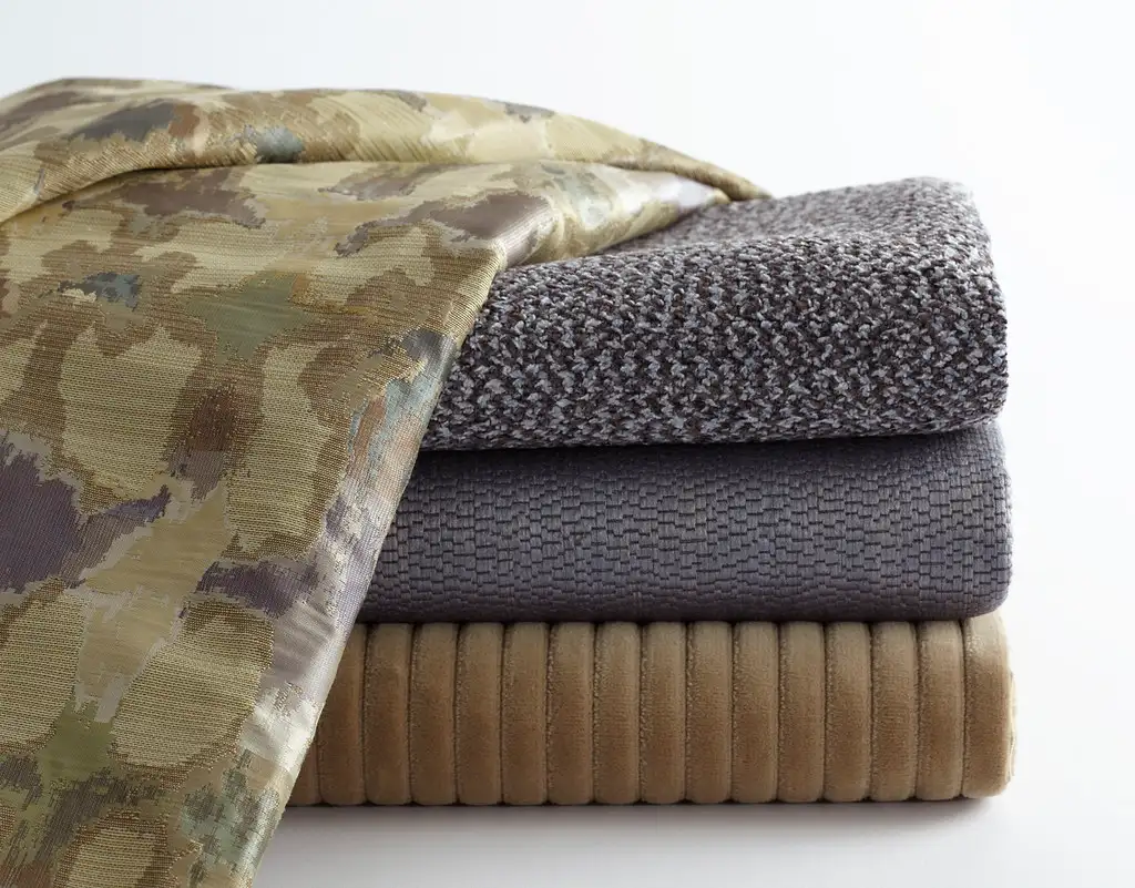 A hand spot-cleans a fabric sofa with spray cleaner and a microfiber cloth.
