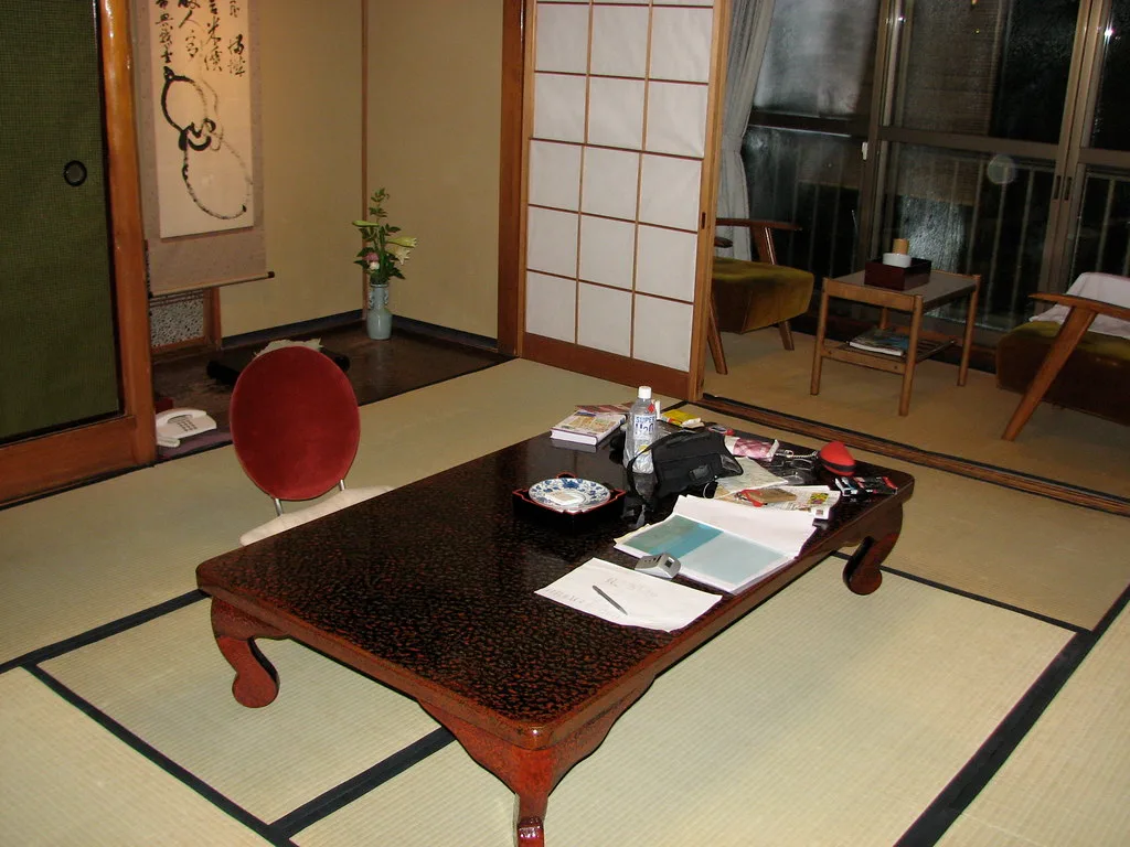 Full futon and queen futon side by side in a small living room with a measuring tape on the floor