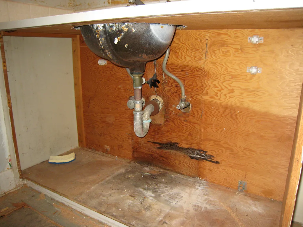 Plumber reconnecting drain pipes under a bathroom vanity.