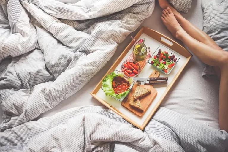 Romantic breakfast in bed for two on a tray with eggs, croissants, berries, juice, and flowers