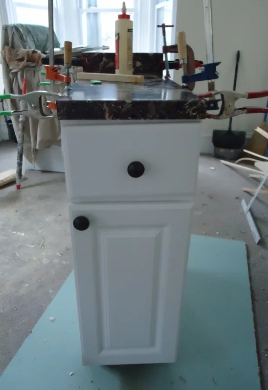 Unfinished kitchen with IKEA kitchen cabinets parts, hardware, and measuring tape in natural light
