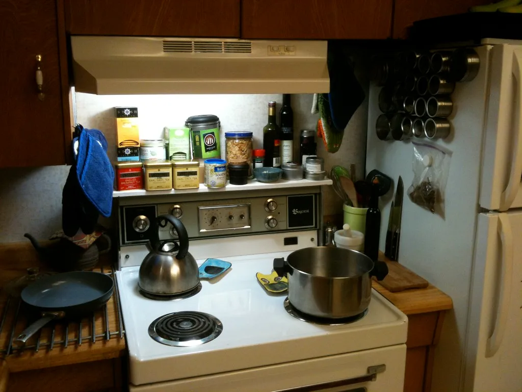 Parent and child compare stainless steel, ceramic, and silicone cookware in a bright kitchen.