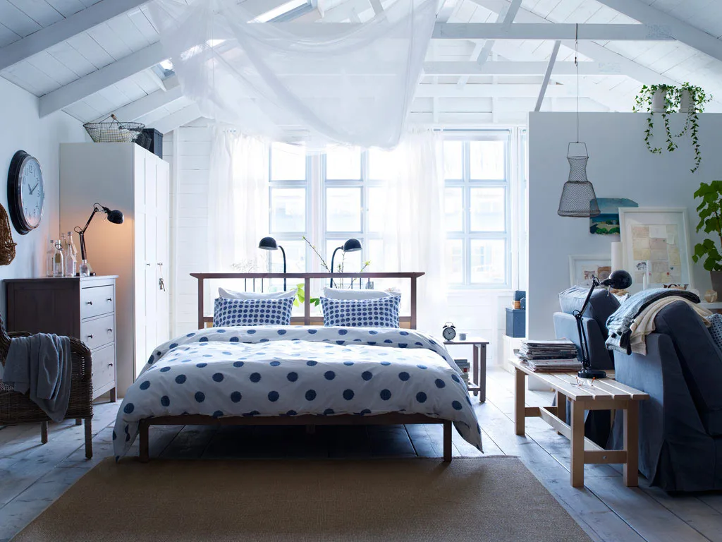 A close-up of a cozy bed corner with linen bedding, a throw, pillows, and a wooden tray.