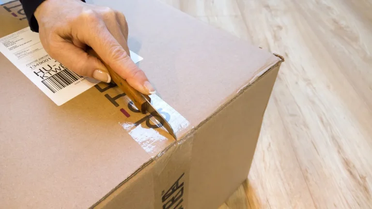 Household goods packed beside a flat rate box and shipping scale on a dining table