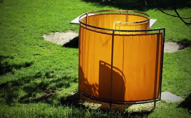 Small balcony with a privacy screen beside outdoor curtains, plants, and neighboring buildings in daylight