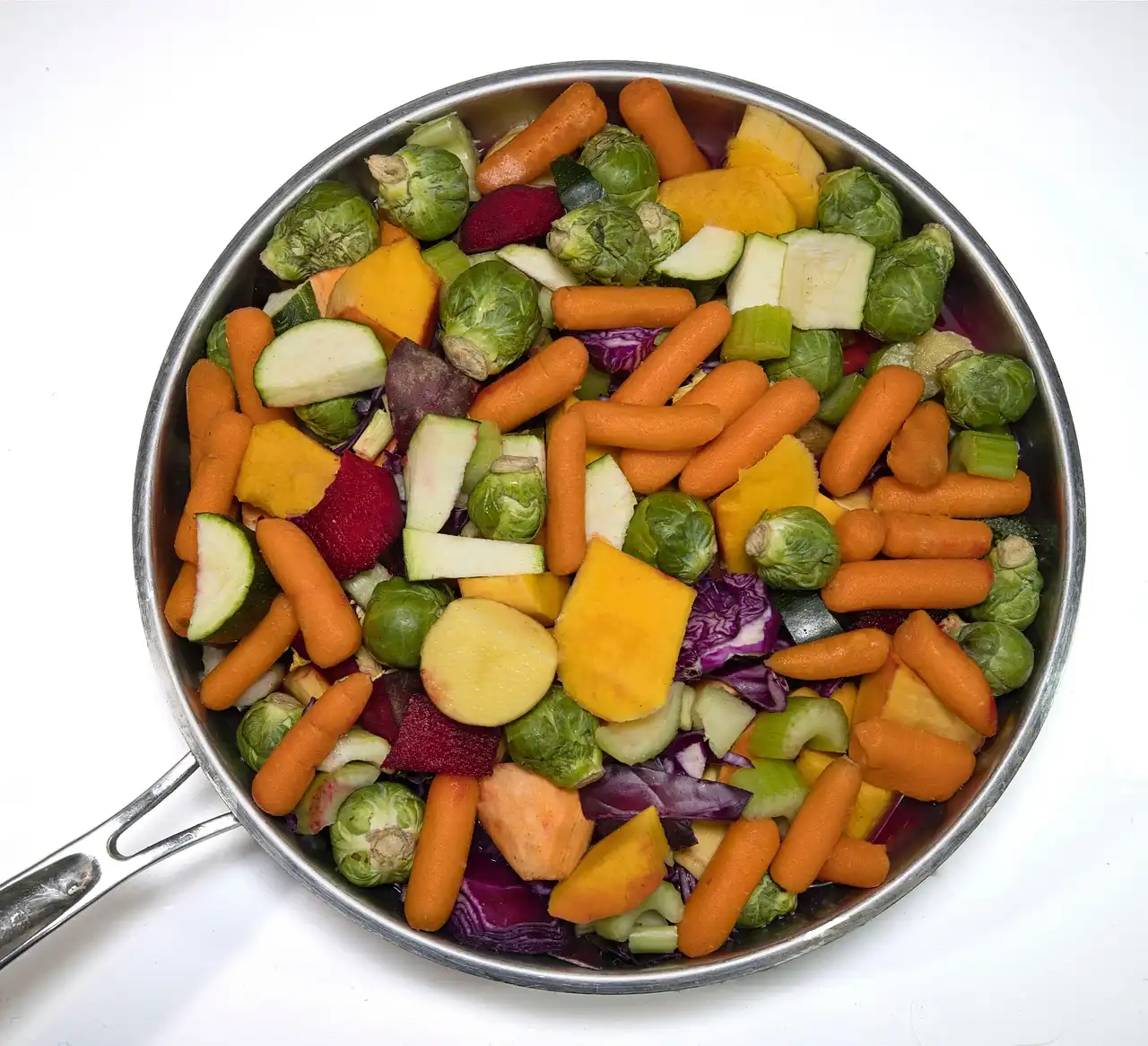 Stainless steel roasting pan on a kitchen counter beside a roast and vegetables