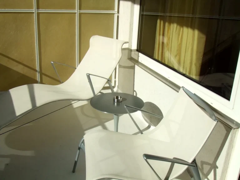 Wood balcony furniture and metal balcony furniture on a sunlit balcony with plants and railing