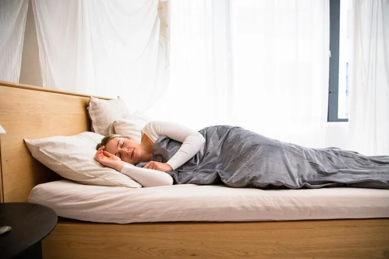 A Zinus bed frame in a small apartment bedroom with a person testing for stability.